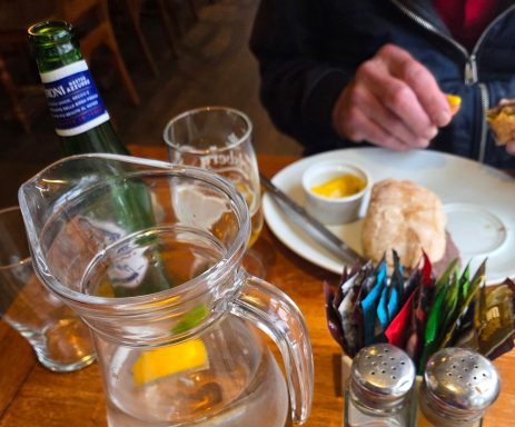 A dining table setting with water, a bowl of sauce, bread, and a person's hand eating food.