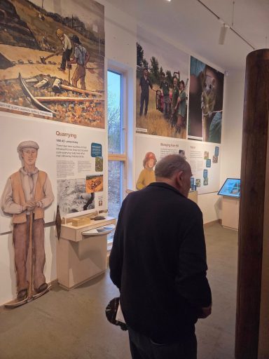 A visitor stands in an exhibition, viewing historic displays and artwork on the walls.